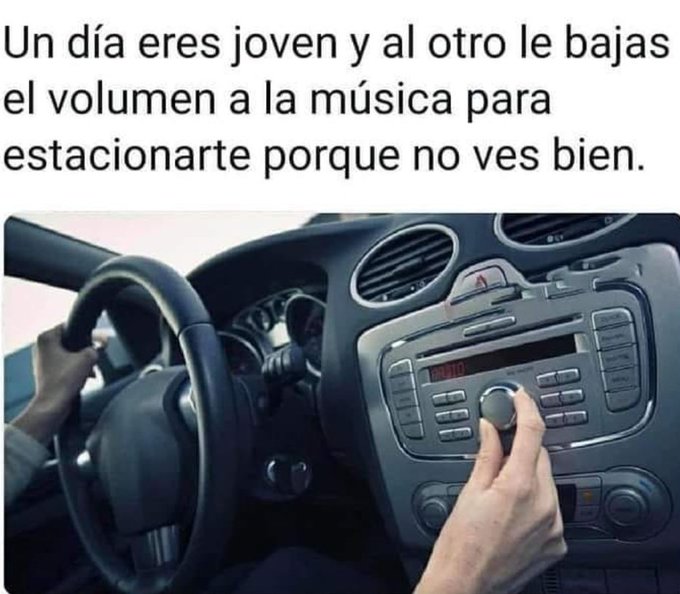 Mano bajando el volumen de la radio del salpicadero de un coche mientras la otra sujeta el volante.