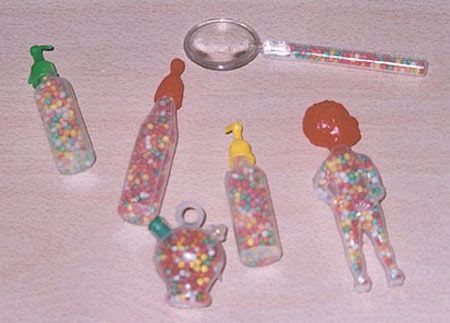 Envases de plástico con forma de biberón, muñeco y cuchara llenos de bolitas de anís de colores.