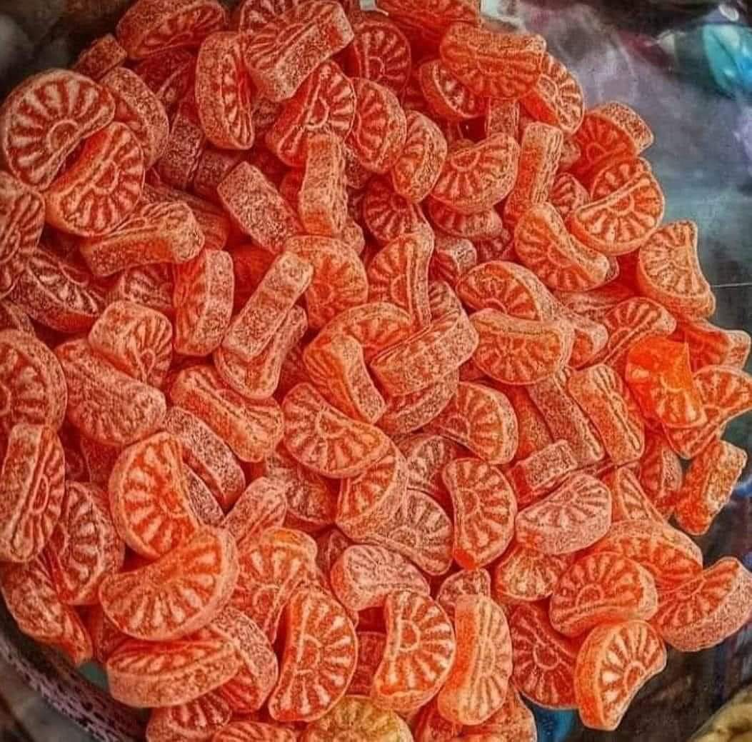Montón de caramelos con forma de gajo de naranja cubiertos de azúcar.