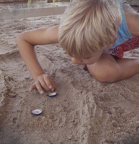 Niño jugando a las chapas en la arena.