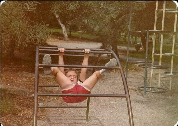Niño colgado cabeza abajo de unas barras metálicas de un parque