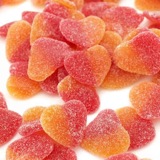 Montón de gominolas con forma de corazón, rojas y naranjas, cubiertas de azúcar.