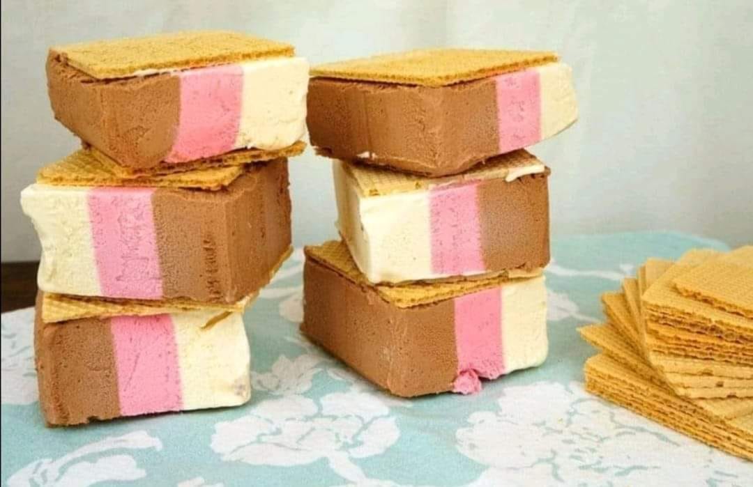 Cortes de helado de tres sabores entre galletas de barquillo apilados en una mesa.