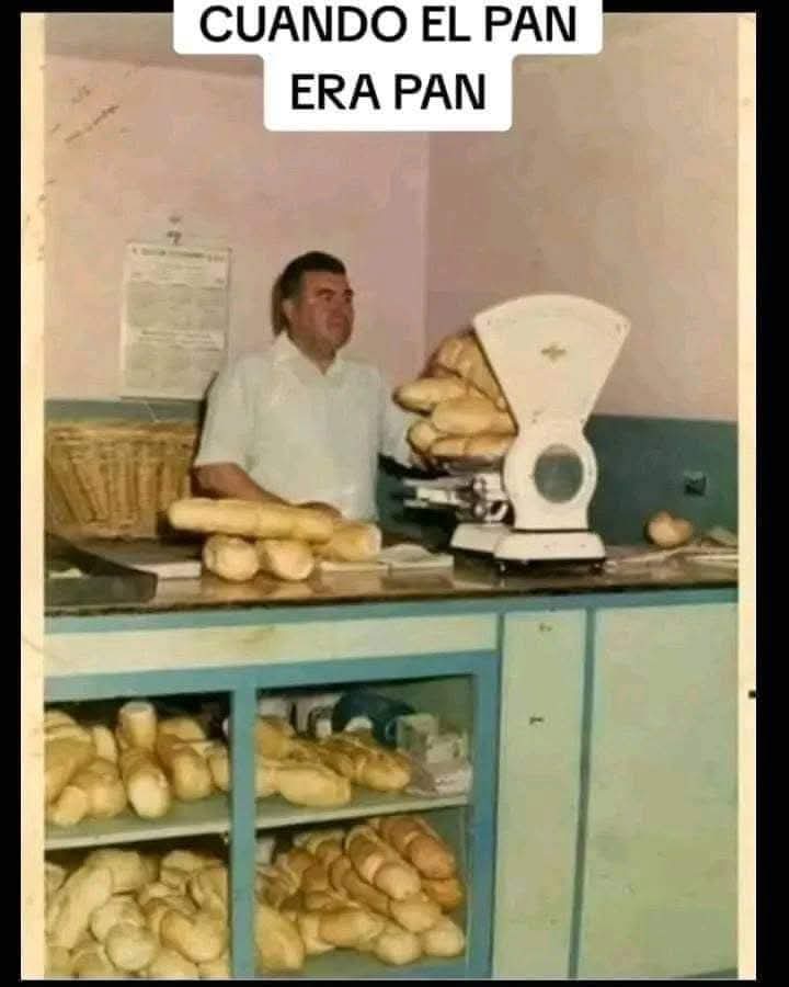Panadero con camisa blanca detrás de un mostrador con una báscula y estanterías llenas de pan.