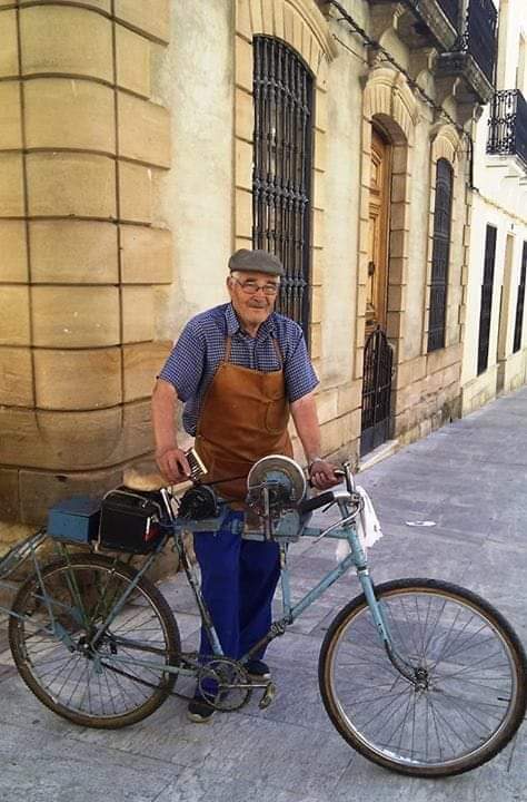 Afilador con delantal junto a su bicicleta en una calle
