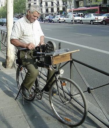 Afilador con su bicicleta afilando en una acera de ciudad