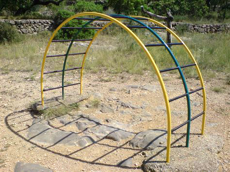 Arco de barras metálicas de colores en un parque.