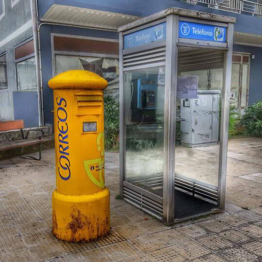Buzón amarillo de Correos junto a una cabina de Telefónica