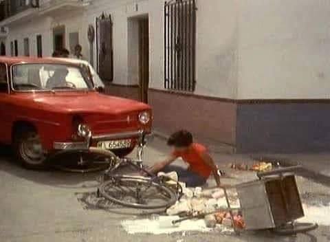 Niño junto a un carrito volcado y un coche rojo en una calle