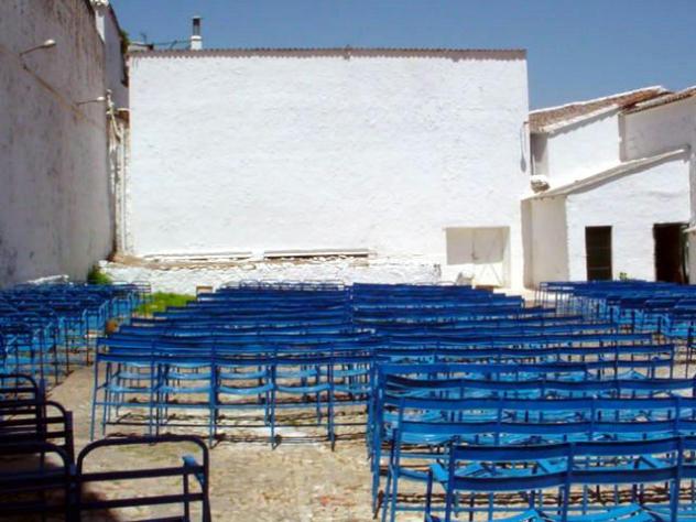 Filas de sillas azules plegables ante una pared blanca en un cine de verano