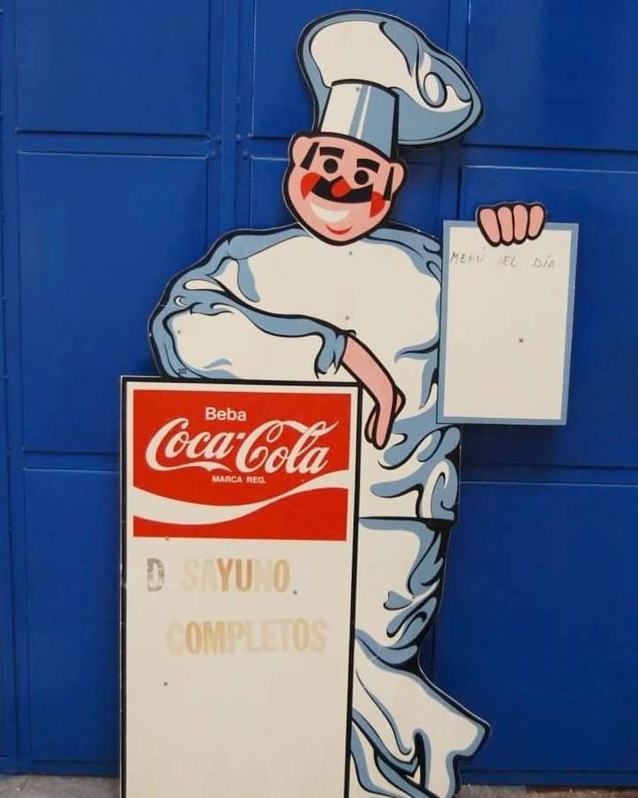 Cartel de cocinero con pizarra y anuncio de Coca-Cola.