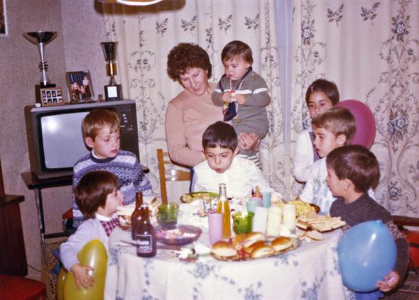 Familia celebrando un cumpleaños infantil con globos y una tele al fondo