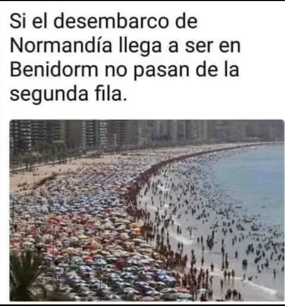 Playa de Benidorm llena de sombrillas de colores y bañistas, con rascacielos al fondo.