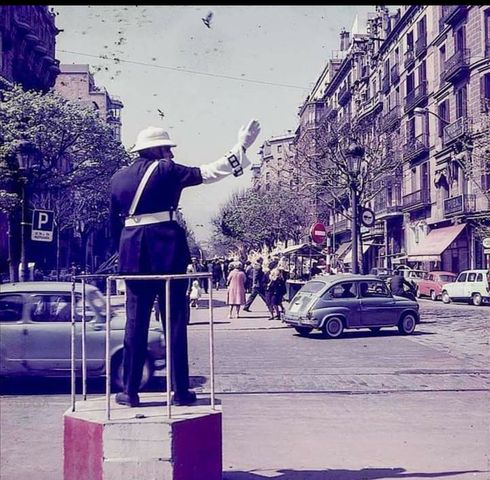 Guardia urbano dirigiendo el tráfico desde una tarima en una calle con coches antiguos