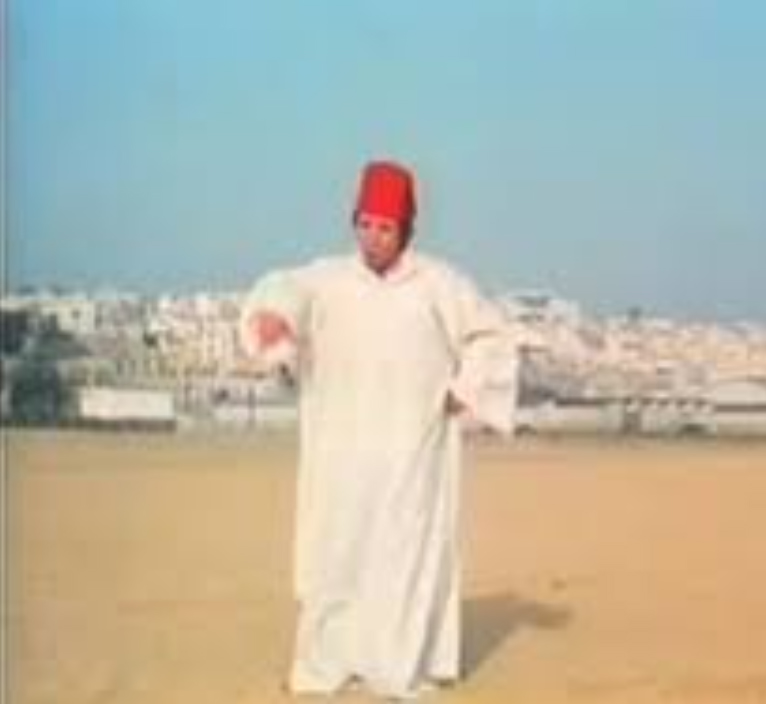 Hombre con chilaba blanca y fez rojo en una playa