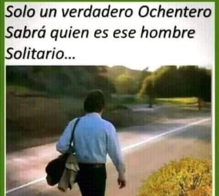 Hombre de espaldas con camisa azul caminando solo por una carretera con una bolsa al hombro.