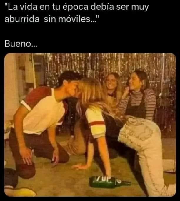 Foto antigua de jóvenes sentados en el suelo alrededor de una botella de 7UP mientras dos de ellos se besan.
