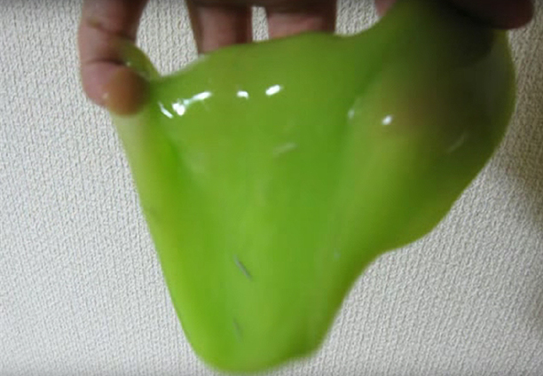 Mano estirando una masa verde y viscosa de juguete.