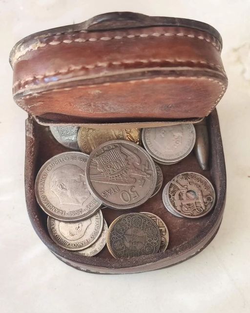 Monedero de cuero abierto lleno de monedas de pesetas.