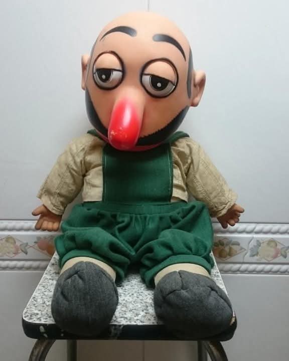 Muñeco con nariz roja y peto verde sentado en una silla