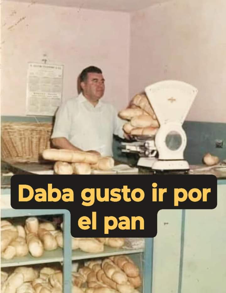 Panadero con camisa blanca detrás del mostrador junto a una báscula y estanterías llenas de pan.