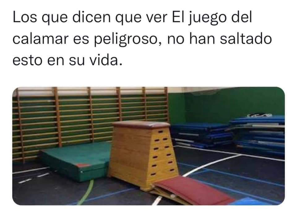 Gimnasio de colegio con un plinto de madera, un trampolín rojo delante, colchonetas verdes y azules y espalderas de madera en la pared.