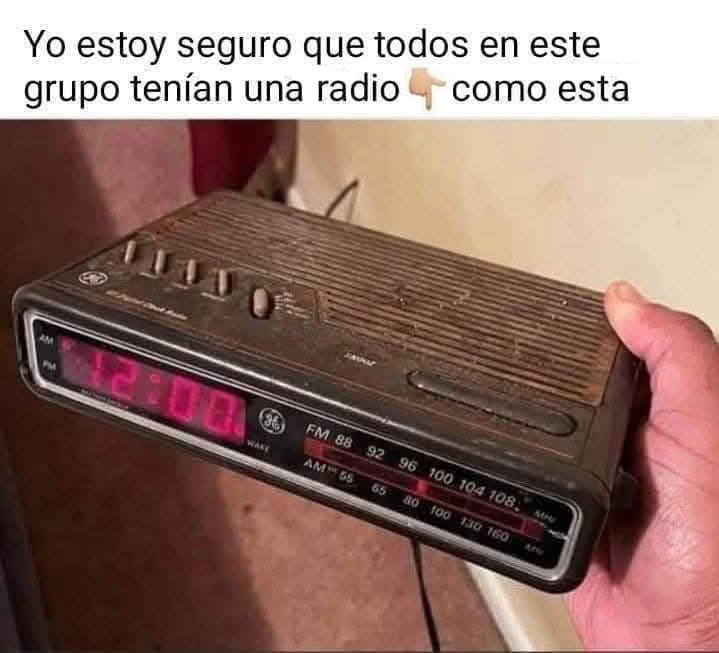 Radiodespertador antiguo negro con los números rojos marcando las 12:00, sujeto por una mano.