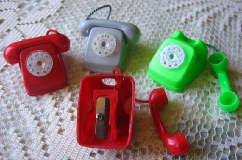 Sacapuntas de plástico con forma de teléfono de disco en rojo, gris y verde.