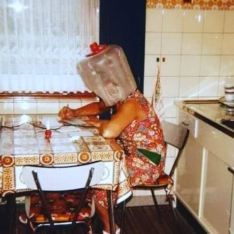 Mujer sentada en una cocina con un secador de capucha de plástico en la cabeza.