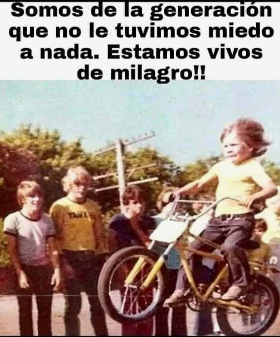 Foto antigua de un niño haciendo el caballito con una bicicleta amarilla ante un grupo de chavales.