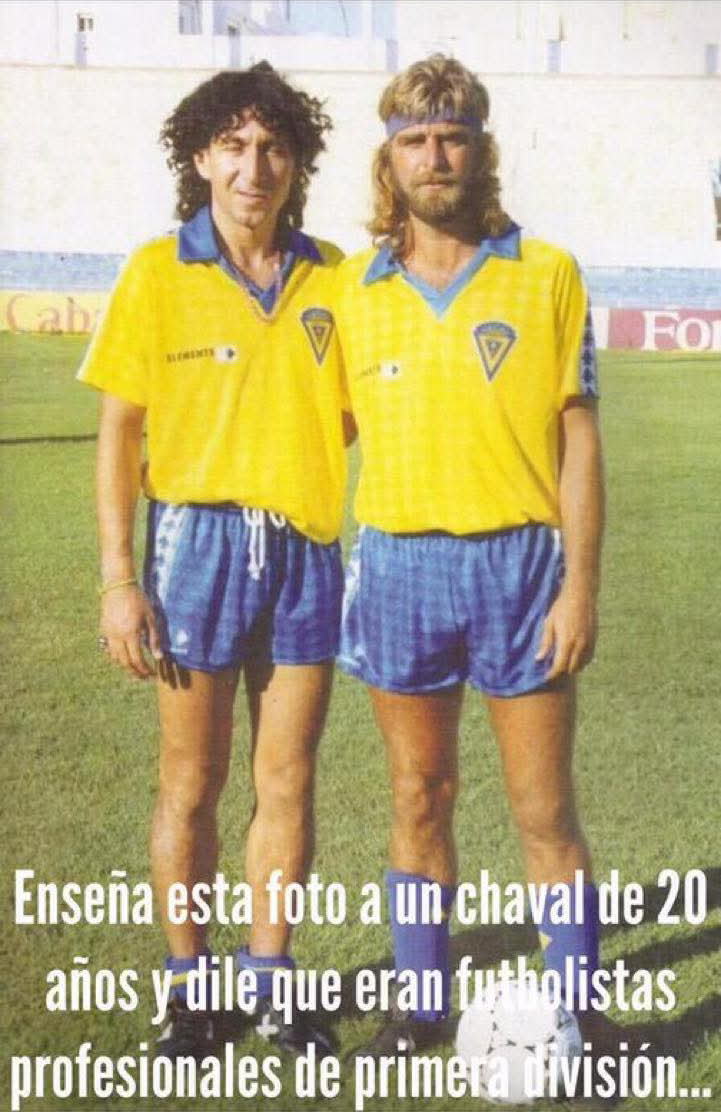 Dos futbolistas con la camiseta amarilla del Cádiz, uno de pelo rizado y otro rubio con melena, barba y cinta en la frente.