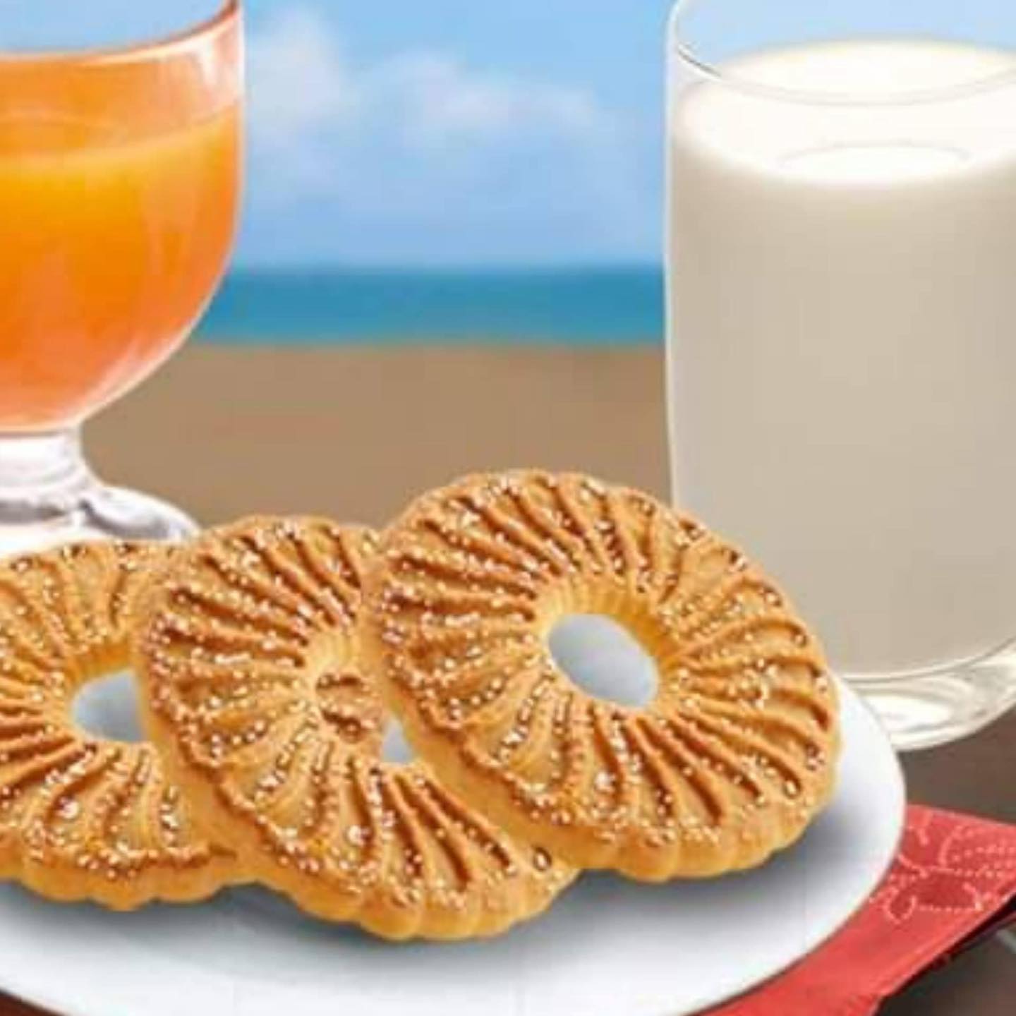 Galletas redondas con agujero y azúcar junto a un vaso de leche y uno de zumo.