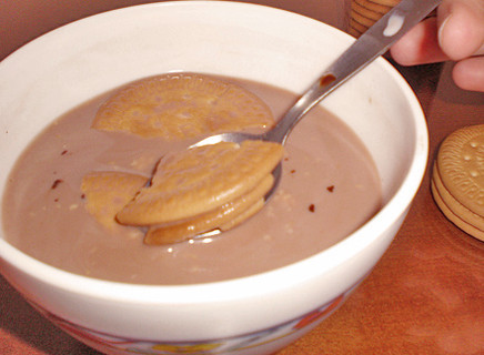 Tazón con galletas María mojadas en leche con cacao y una cuchara.