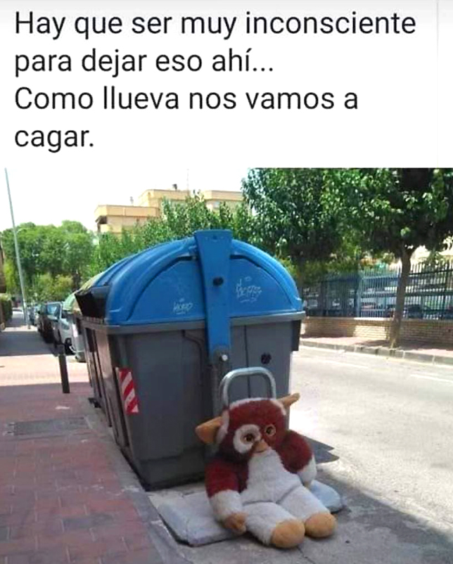 Peluche de Gizmo, marrón y blanco, sentado en la acera junto a un contenedor de basura gris con tapa azul.