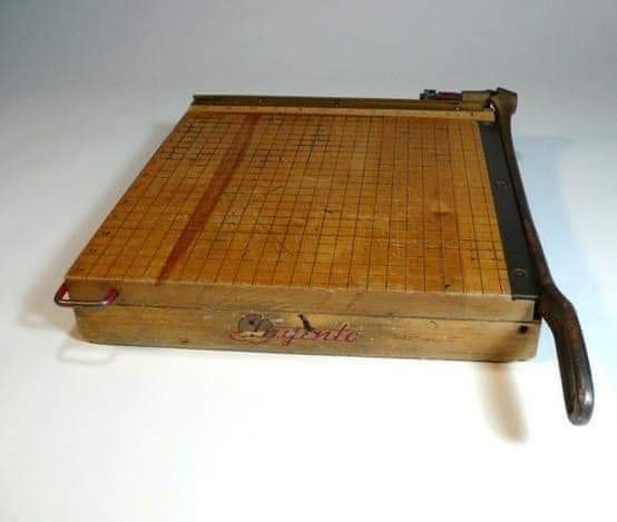 Guillotina de papel antigua con tablero de madera cuadriculado y cuchilla de hierro con mango.