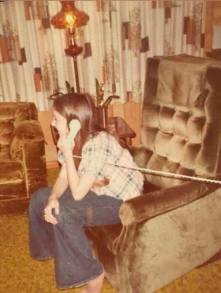 Chica hablando por un teléfono de cable sentada en un sillón de terciopelo