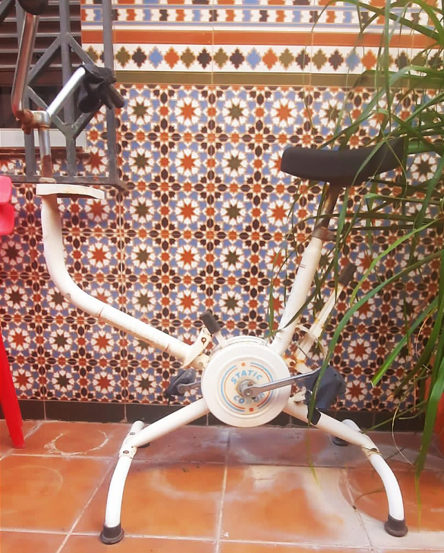 Bicicleta estática blanca en un patio con azulejos