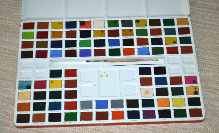Caja metálica abierta de acuarelas con muchas pastillas de colores y un pincel.
