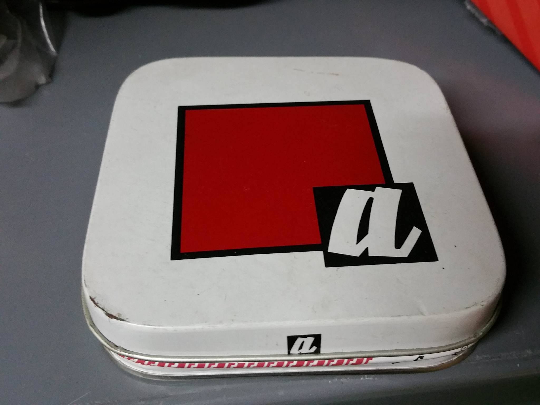 Caja de lata blanca con un cuadrado rojo.