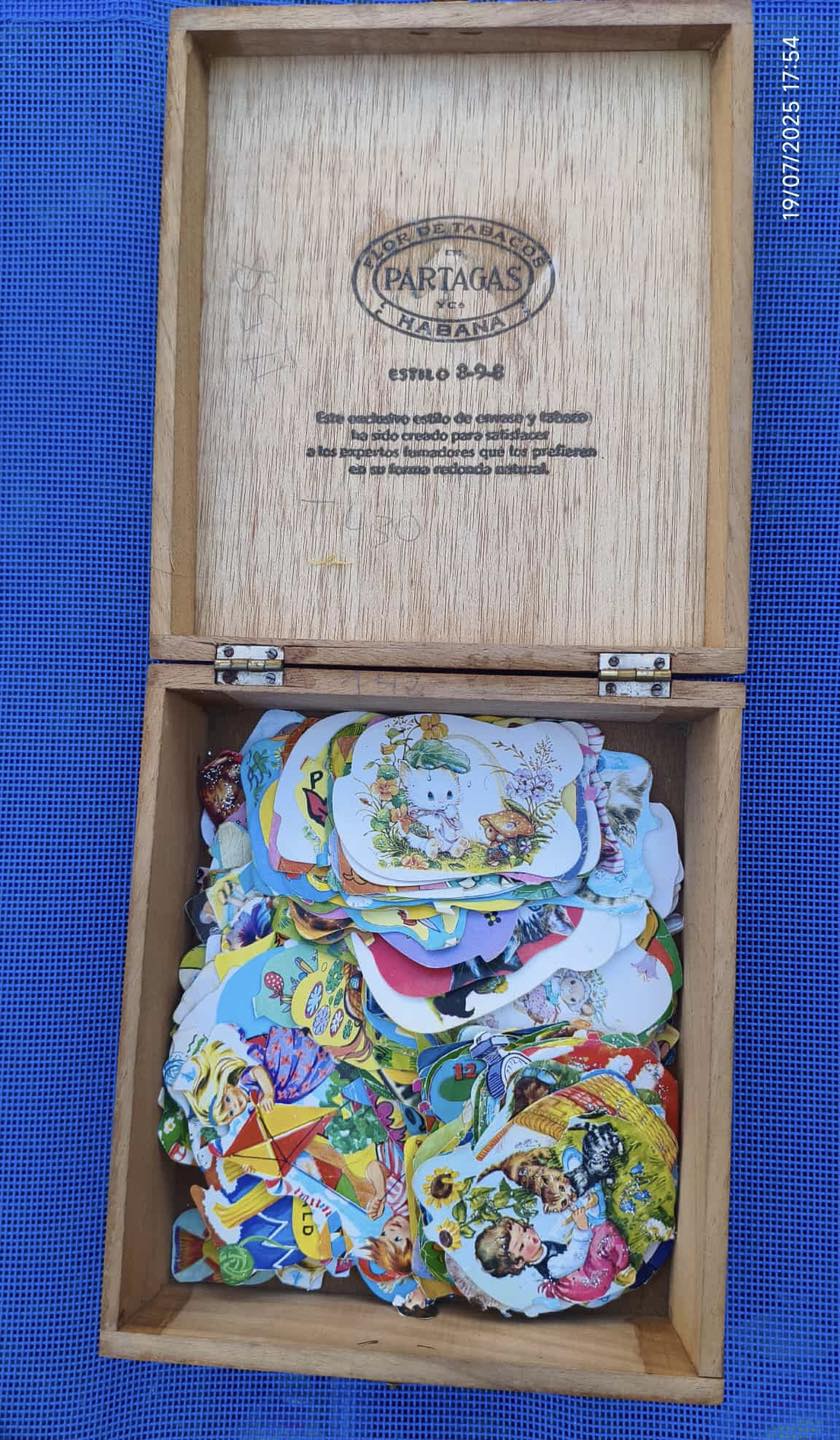 Caja de puros de madera abierta llena de cromos troquelados de colores.