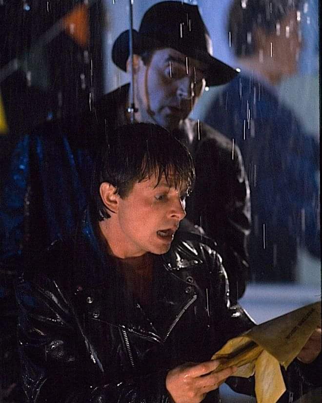 Mujer leyendo una carta bajo la lluvia con un hombre con sombrero detrás