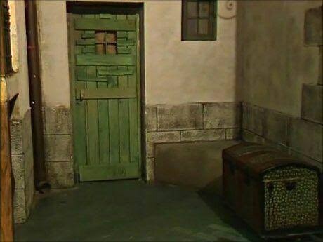 Puerta verde de madera en un sótano de piedra con un baúl al lado.
