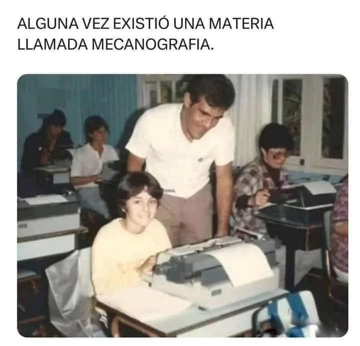 Clase antigua de mecanografía con alumnos escribiendo a máquina y un profesor de pie junto a una alumna.