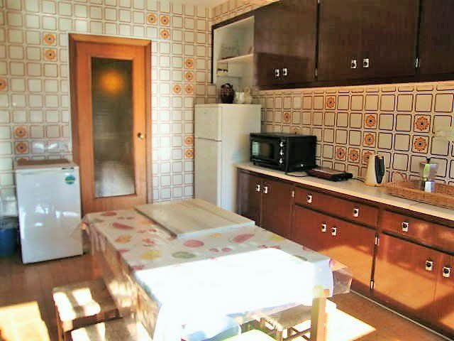 Cocina antigua con azulejos de dibujos naranjas y marrones, muebles de madera oscura y una mesa con hule.