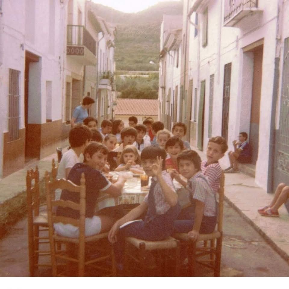 Niños sentados en una mesa larga en una calle de pueblo