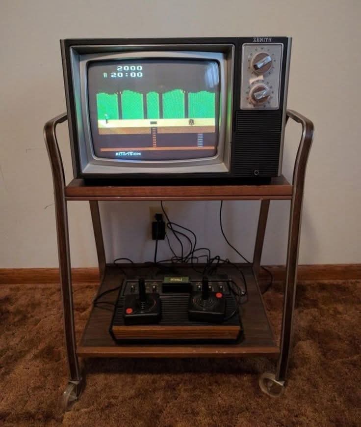 Consola Atari con mandos sobre un carrito bajo un televisor