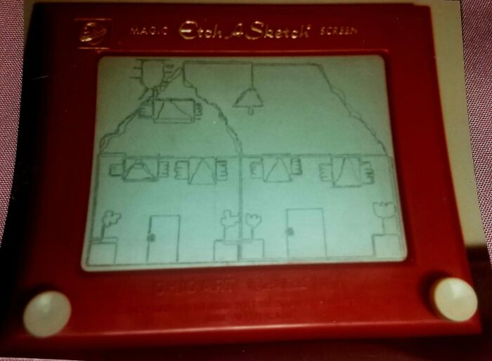 Pizarra mágica roja Etch A Sketch con el dibujo de una casa hecho con líneas.
