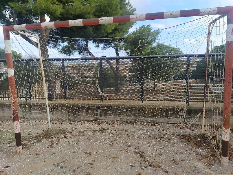 Portería de fútbol de hierro con la red rota en un campo de tierra.