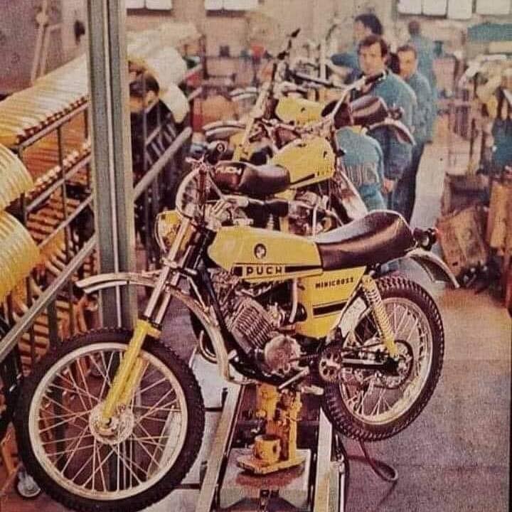 Cadena de montaje con varias motos Puch Minicross amarillas en fila y operarios trabajando al fondo.