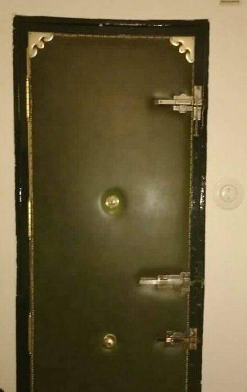 Puerta metálica verde de un piso antiguo con mirilla y cerrojos